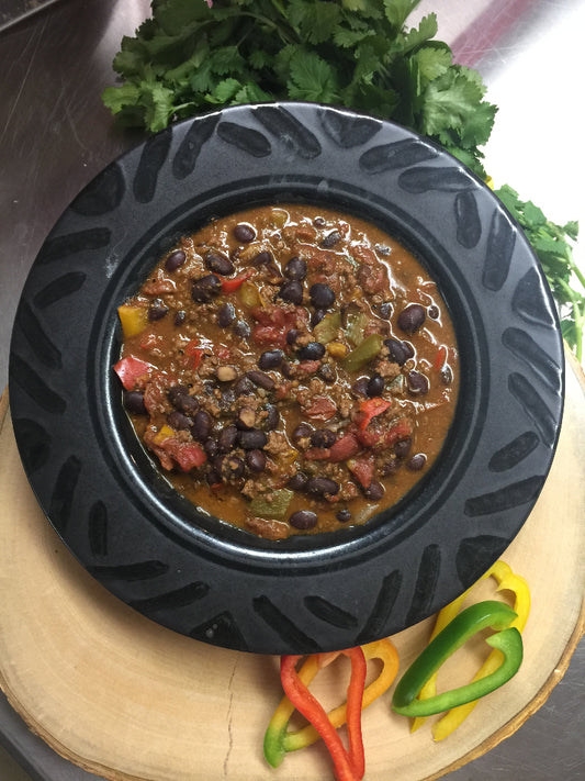 Black bean chili in a black bowl on a wooden surface with bell peppers and cilantro.