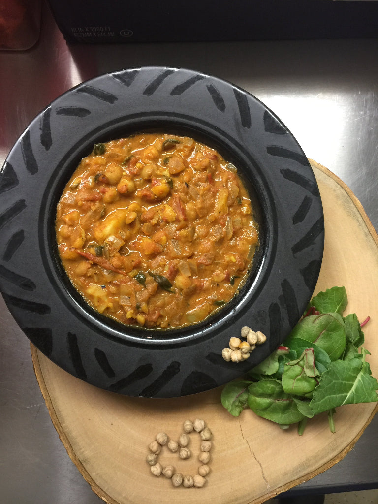 Black bowl with a coconut chickpea curry on a wooden plate